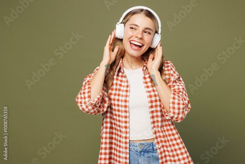 Young fun woman she wear red shirt white t-shirt casual clothes listen to music in headphones look aside on area mock up isolated on plain pastel green background studio portrait. Lifestyle concept.