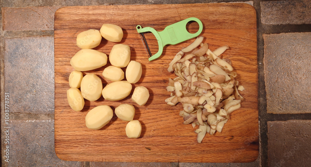 Fototapeta premium peeled potatoes, peeler and peelings on a wooden cutting board