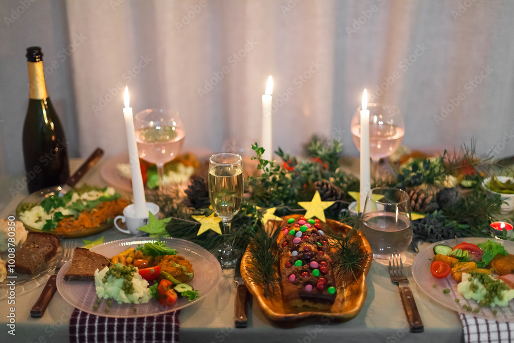 Christmas feast table with plates of food, glasses of wine and champagne, with festive decorations of pinecones, golden stars paper garland and long candles in evergreen foliage centerpieces Christmas feast table with plates of food, glasses of wine and champagne, with festive decorations of pinecones, golden stars paper garland and long candles in evergreen foliage centerpieces