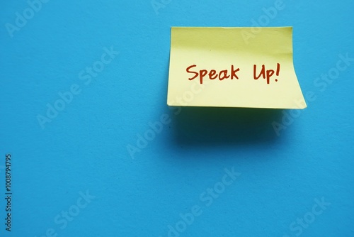 Yellow note stick on copy space blue background with text written SPEAK UP !, to raise voice louder - dare to express opinion frankly and openly , stand up for yourself