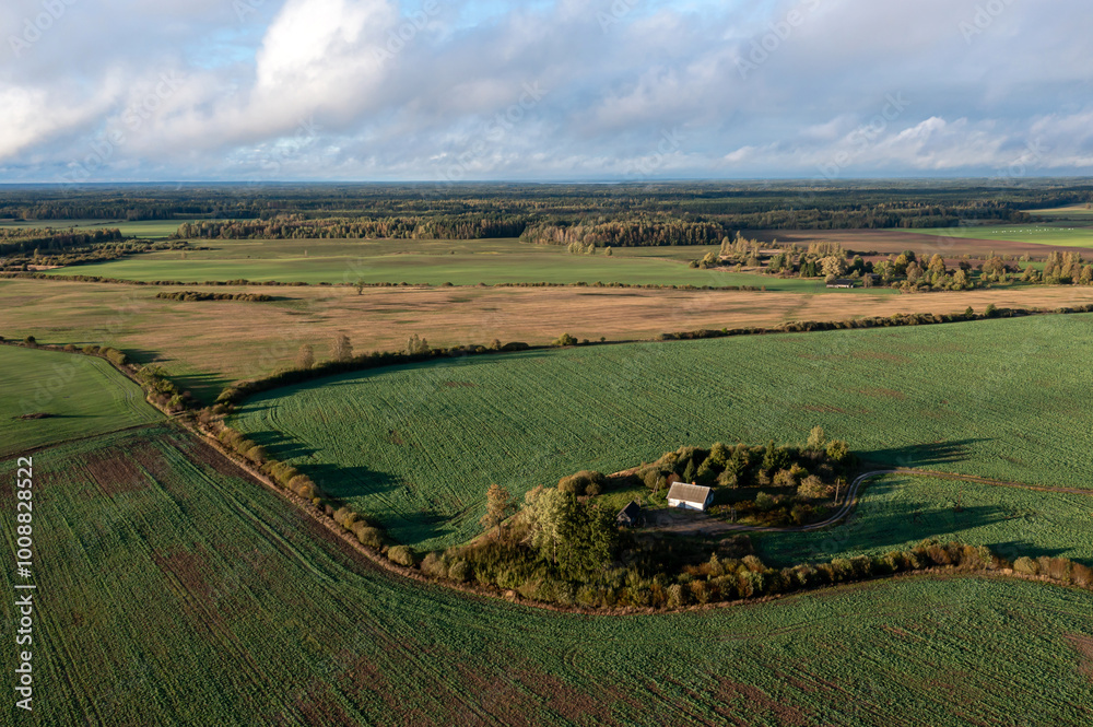 Fototapeta premium Aerial view of a secluded cottage surrounded by vibrant green fields in early morning light