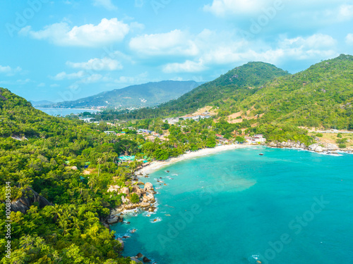 Aerial view of a serene tropical beach with turquoise waters and lush green hills on a sunny day in a coastal paradise