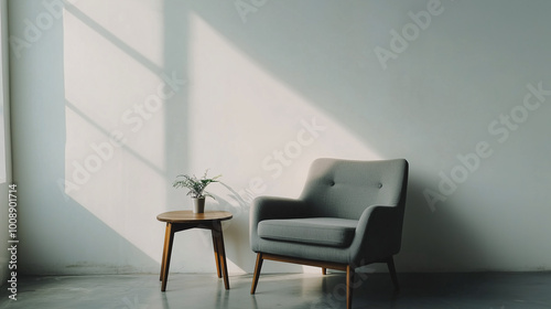 Elegant minimalist living space with a comfortable accent chair and a small wooden side table, placed against a plain white wall. The focus is on simple, functional design