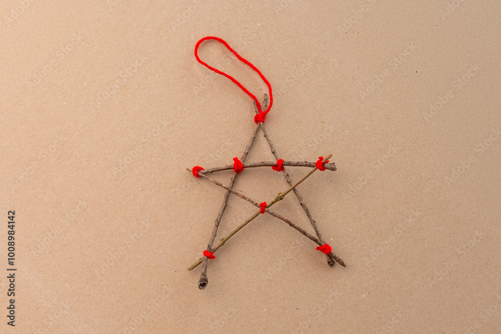 Fototapeta premium a five-pointed star crafted from sticks, tied together at the points with red string. The star has a rustic, handmade look, making it a charming addition to holiday decorations or craft projects.