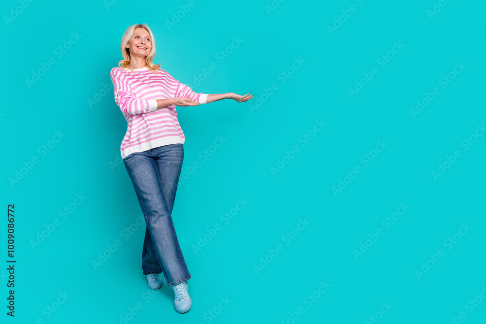 Full length photo of cheerful retired person wear striped pullover look empty space arm hold product isolated on blue color background Full length photo of cheerful retired person wear striped pullover look empty space arm hold product isolated on blue color background