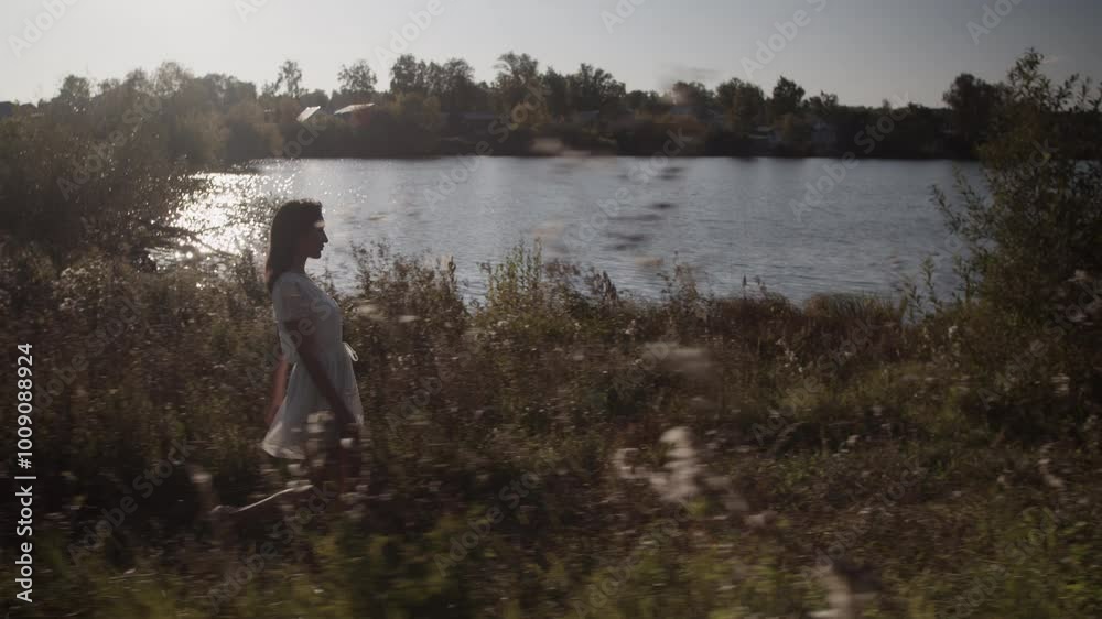 Young woman walking along lakeside in nature in sundown time Young woman walking along lakeside in nature in sundown time