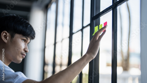 Man organizing project tasks Colorful sticky notes on glass of meeting room