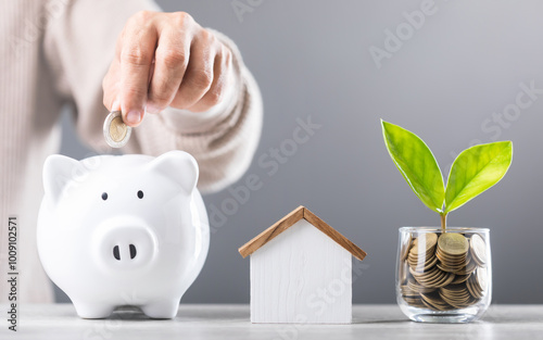 A Man drops coins into white piggy bank, glass jar of coin and a wooden house model beside him. Emphasizes the concept of saving money for future house investments and financial stability photo