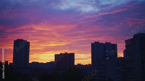 Vibrant orange and purple sunset over a city skyline, with tall apartment buildings silhouetted against the sky.