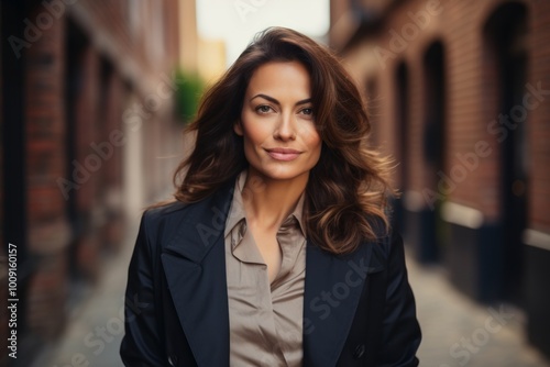 Portrait of a glad woman in her 40s dressed in a stylish blazer in front of vintage brick wall