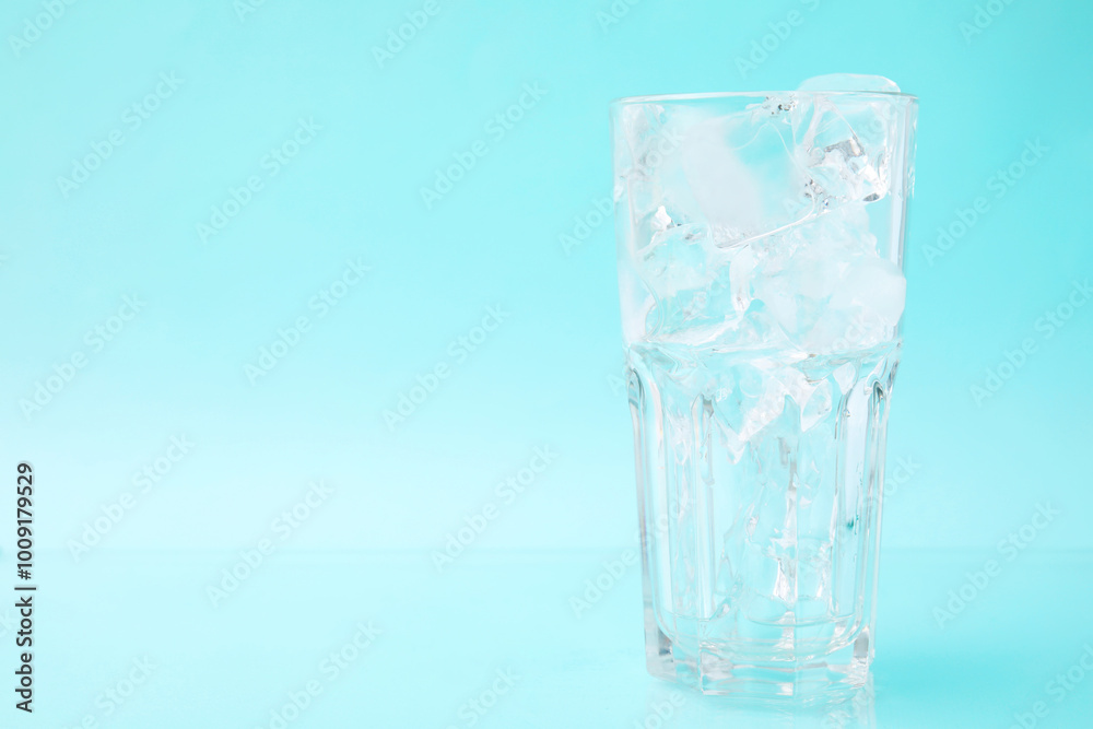 Refreshing water with ice cubes in glass on light blue background, space for text Refreshing water with ice cubes in glass on light blue background, space for text
