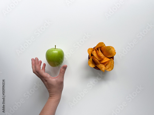 Woman chooses a green apple over unhealthy potato chips. Hand reaches out to healthy fruit instead of snacks.