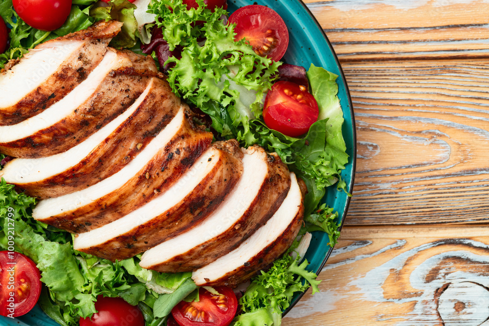 Grilled chicken breast ( fillet ) with lattuce salad and cherry tomatoes . Top view Grilled chicken breast ( fillet ) with lattuce salad and cherry tomatoes . Top view