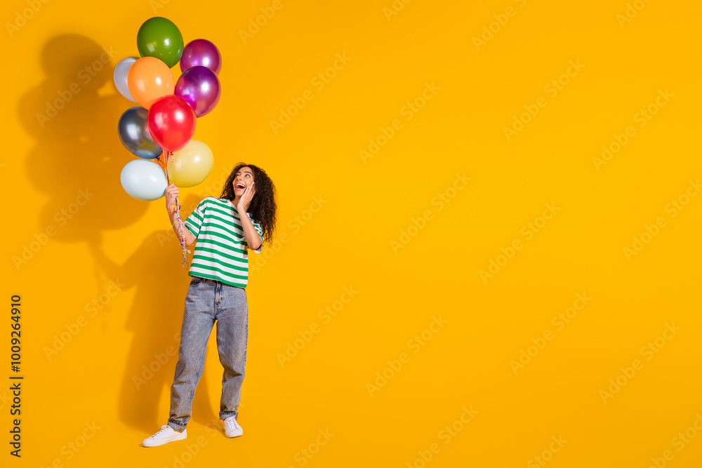 Full size photo of pretty young girl balloons empty space wear striped t-shirt isolated on yellow color background Full size photo of pretty young girl balloons empty space wear striped t-shirt isolated on yellow color background