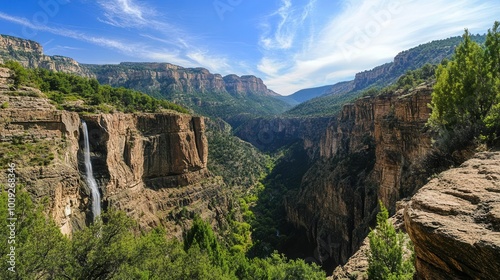 A breathtaking view of a canyon with a waterfall surrounded by lush greenery and mountains.