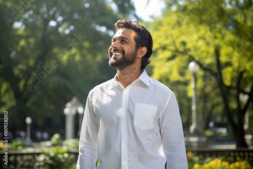 Portrait of a blissful indian man in his 30s wearing a classic white shirt isolated on vibrant city park