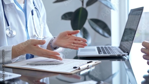 Doctor woman is writing something while consulting man patient on the glass desk and a clipboard in medical office. Medicine concept