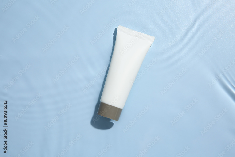 Cosmetic product. Tube with cream in water on light blue background, top view Cosmetic product. Tube with cream in water on light blue background, top view