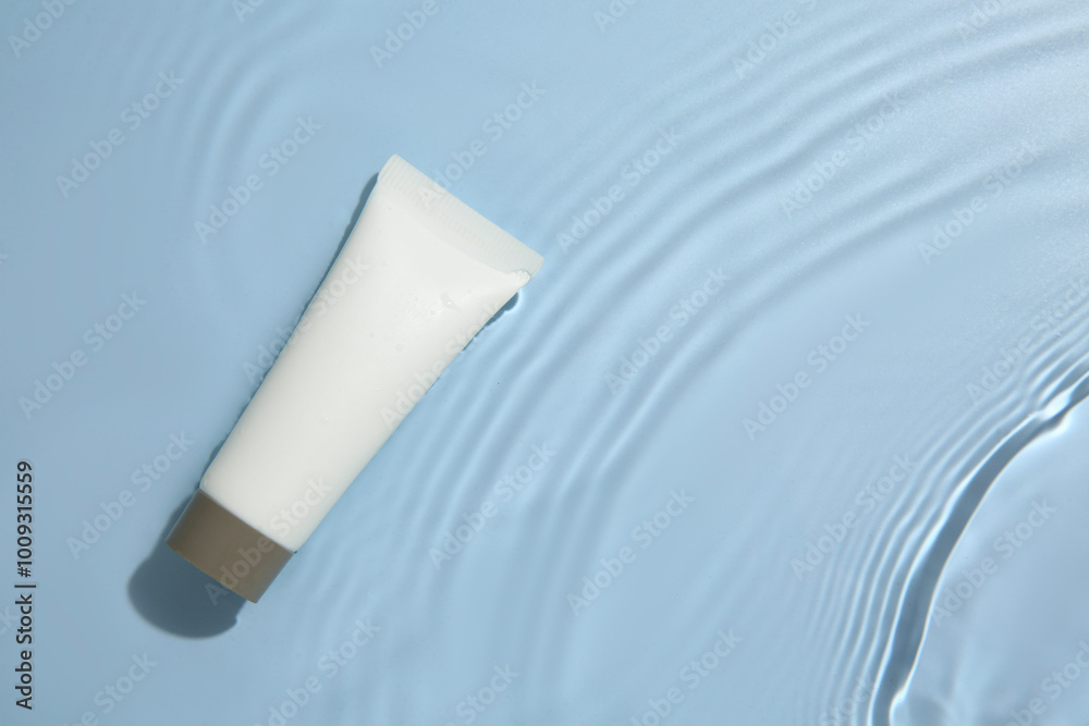 Cosmetic product. Tube with cream in water on light blue background, top view. Space for text Cosmetic product. Tube with cream in water on light blue background, top view. Space for text