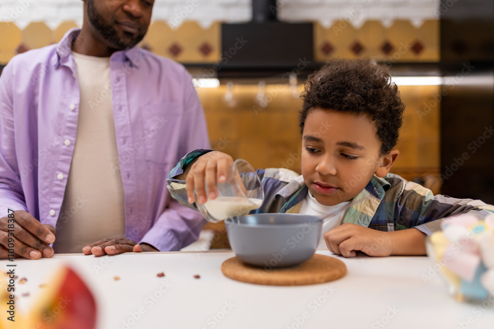 Cute african american boy eating breakfast, his dad sitting near Cute african american boy eating breakfast, his dad sitting near