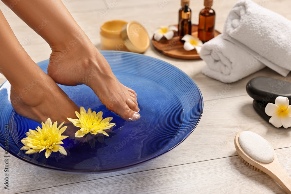 Woman soaking her feet in bowl with water and flowers on floor, closeup. Body care Woman soaking her feet in bowl with water and flowers on floor, closeup. Body care