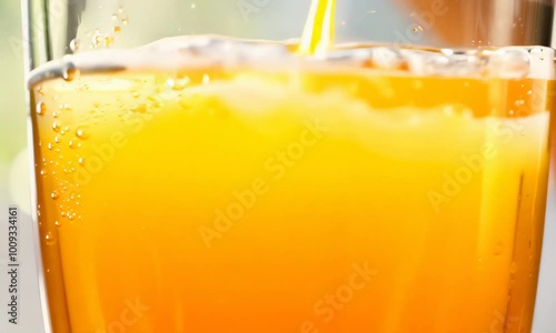Close up shot of orange juice being poured into a glass  creating bubbles and foam.