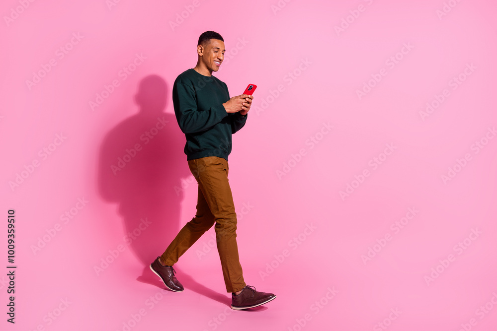 Full length photo of cheerful positive guy dressed pullover typing modern device emtpy space isolated pink color background Full length photo of cheerful positive guy dressed pullover typing modern device emtpy space isolated pink color background