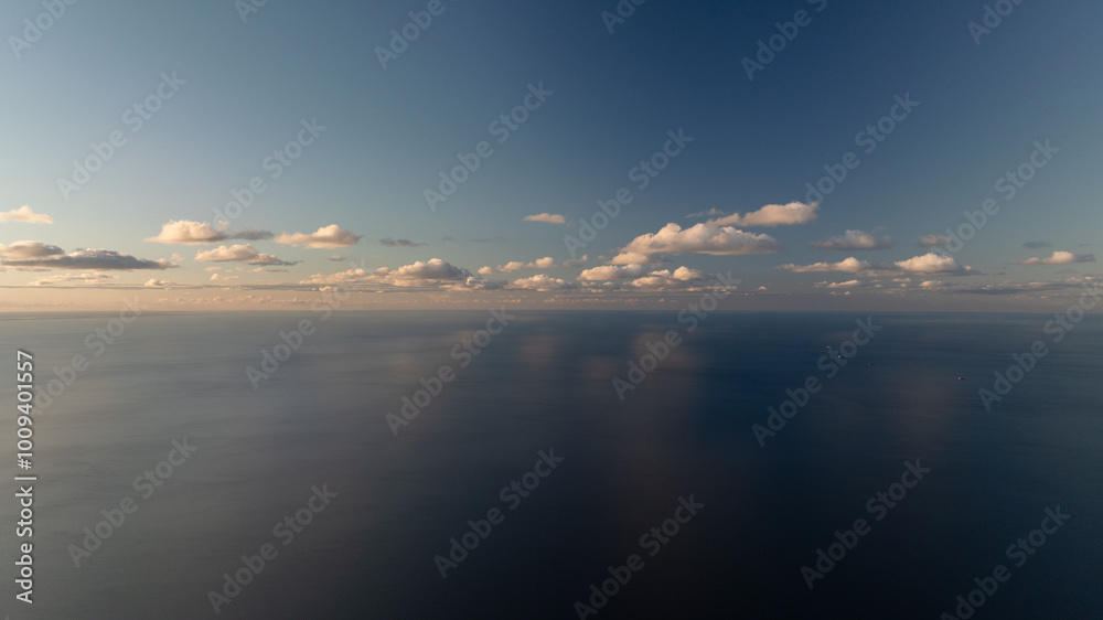 A scene of a tranquil body of water dotted with clouds, overhead flies a plane against a clear blue sky A scene of a tranquil body of water dotted with clouds, overhead flies a plane against a clear blue sky