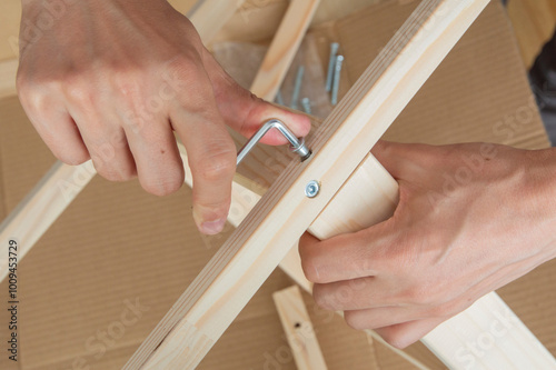 close-up： one hand holds a hex key in a confirmat screwed into a wooden table leg, the other hand holds a wooden table leg