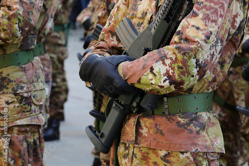 hands with black gloves of army soldier in camouflage suit while holding a black rifle during military parade photo