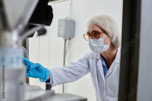 Quadro em tela Side view of female technician in protective mask and hairnet inspecting tablet