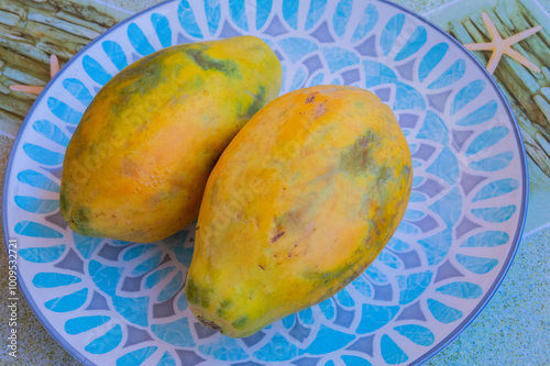 close-up: two big orange hue ripe fruits of papaya on a turquois blue plate with rhombus pattern photo