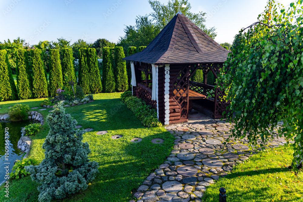 Wooden gazebo nestled in a beautifully landscaped garden. The gazebo has a dark wooden brown exterior. A stone path leads up to the gazebo, inviting to enter and enjoy the peaceful atmosphere. Wooden gazebo nestled in a beautifully landscaped garden. The gazebo has a dark wooden brown exterior. A stone path leads up to the gazebo, inviting to enter and enjoy the peaceful atmosphere.