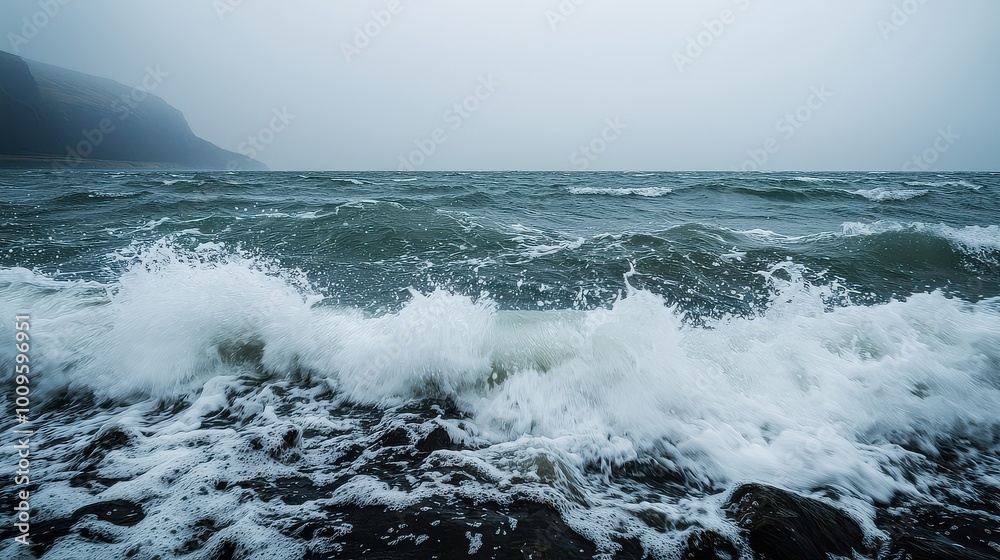 A moody seascape featuring turbulent waves crashing against rocky shores under a foggy, gray sky. A moody seascape featuring turbulent waves crashing against rocky shores under a foggy, gray sky.
