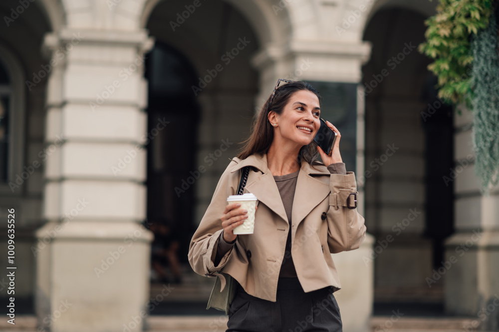 Smiling businesswoman walking and talking on the phone holding coffee Smiling businesswoman walking and talking on the phone holding coffee