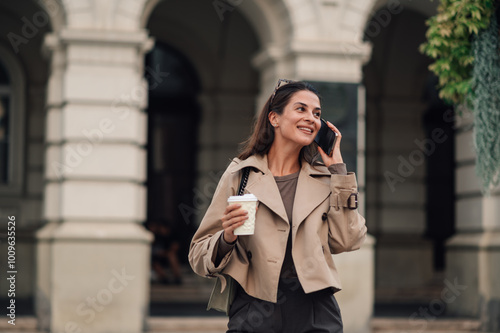 Foto Smiling businesswoman walking and talking on the phone holding coffee