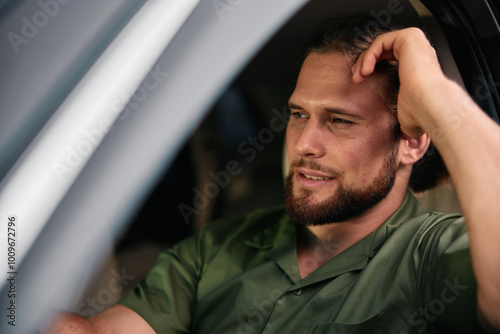 Thoughtful man sitting in a car with a casual expression, wearing a green shirt and looking out the window, reflecting on his thoughts