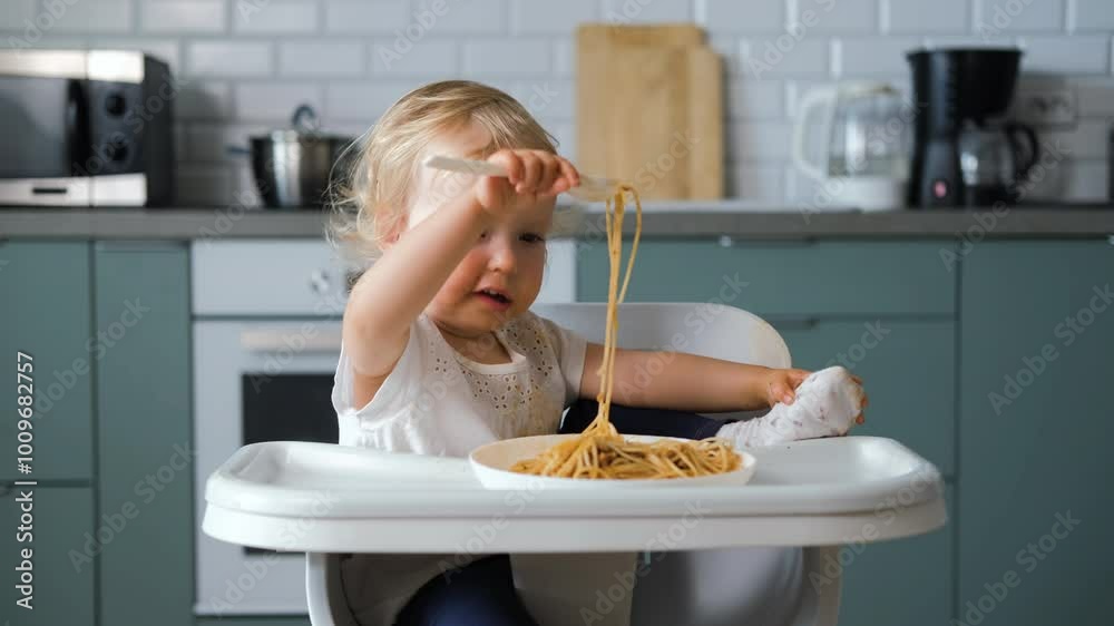 Charming baby sits in a high chair, concentrating on eating pasta bolognese with a fork. The cozy kitchen provides a warm backdrop to this delightful lunchtime Charming baby sits in a high chair, concentrating on eating pasta bolognese with a fork. The cozy kitchen provides a warm backdrop to this delightful lunchtime