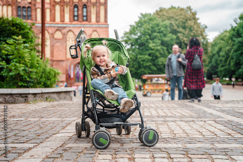 Little child girl toddler sits in a stroller and smiles outside in summer. Kaliningrad, Russia - 18 June 2024