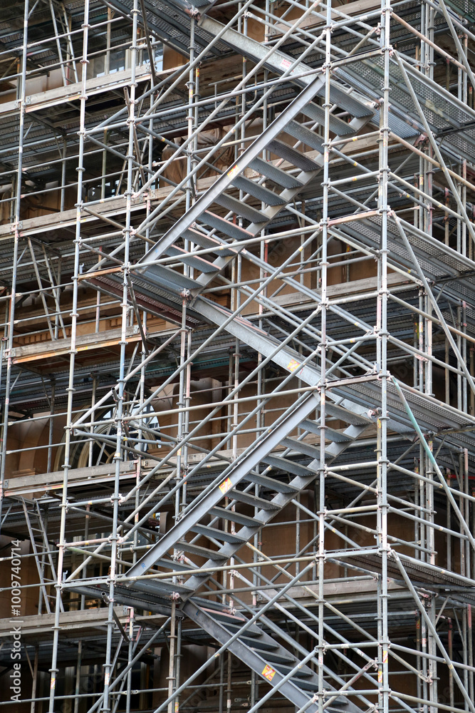 Sturdy steel staircase winds through a complex grid of scaffolding, illustrating the active construction process and the intricate support systems in place for building projects Sturdy steel staircase winds through a complex grid of scaffolding, illustrating the active construction process and the intricate support systems in place for building projects