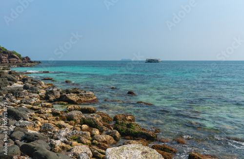 A tourist ship sails past the rocky shore and coral reef of a tropical island