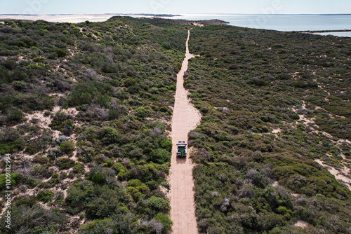 Aerial picture of a 4wd driving on a gravel road in the middle of the bush. Straight road in the middle of nowhere. 4x4 adventure in Western Australia. Sandy road.