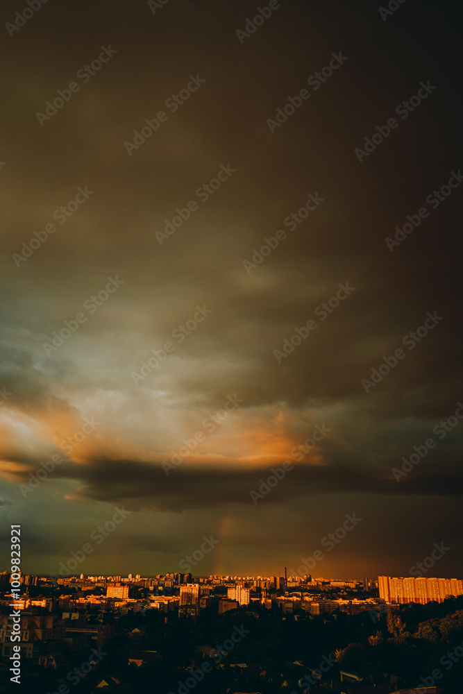 Fototapeta premium rainbow appeared against gray stormy sky over residential area of the city.