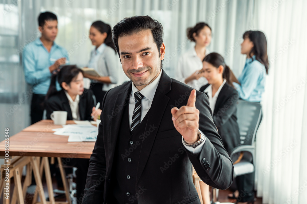Portrait of happy businessman looking at camera, making finger pointing gesture for advertising product with motion blur background of business people movement in dynamic business meeting. Habiliment Portrait of happy businessman looking at camera, making finger pointing gesture for advertising product with motion blur background of business people movement in dynamic business meeting. Habiliment