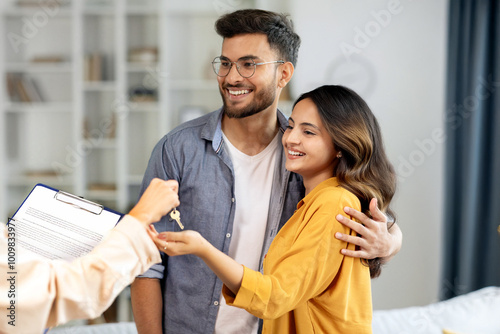 Real estate agent giving keys to young indian buyers, happy woman taking key of future new apartment, spouses buying new house