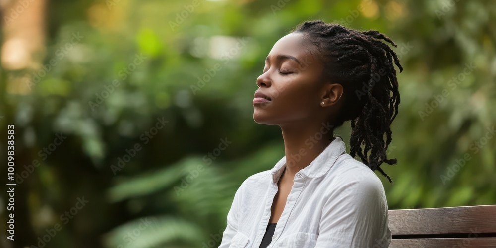 A woman with dreadlocks meditates peacefully in a lush, green environment.