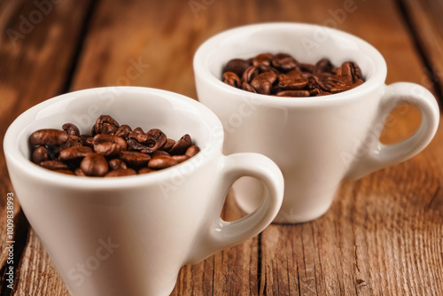 Two white ceramic cups with roasted coffee beans inside on brown wooden table. Coffee shop, caffeine, roast concept. Roasted beans for mass market sale, horizontal photo. photo