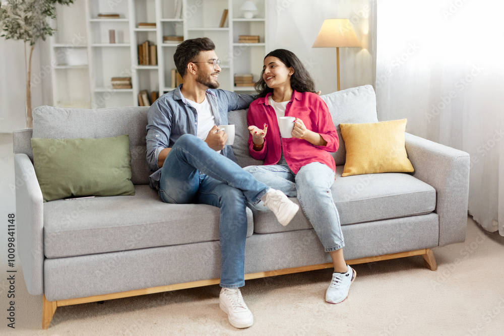 Happy indian couple relaxing and drinking coffee, sitting on couch at home, talking , free space Happy indian couple relaxing and drinking coffee, sitting on couch at home, talking , free space