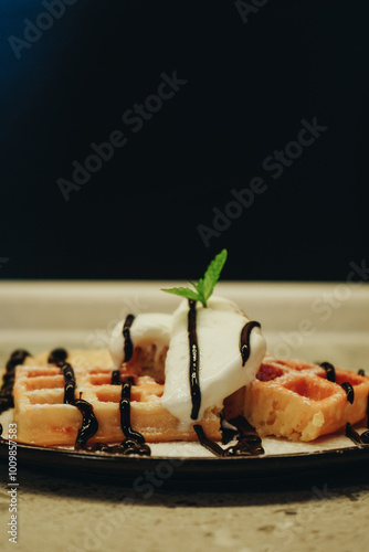 Mint on top of dessert. Served with ice cream. Belgian waffles with banana, ice cream and chocolate on top. Sweet dessert waffles. Delicious dessert for tea time. Cooking process. Dark background.