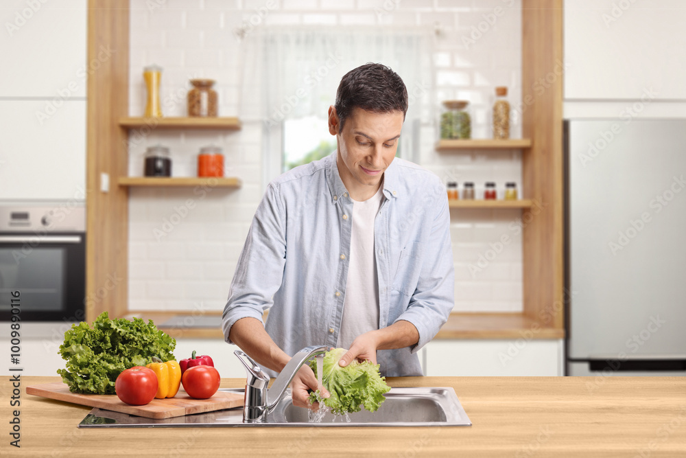 Young man washing lettuce salad in a kitchen sink Young man washing lettuce salad in a kitchen sink